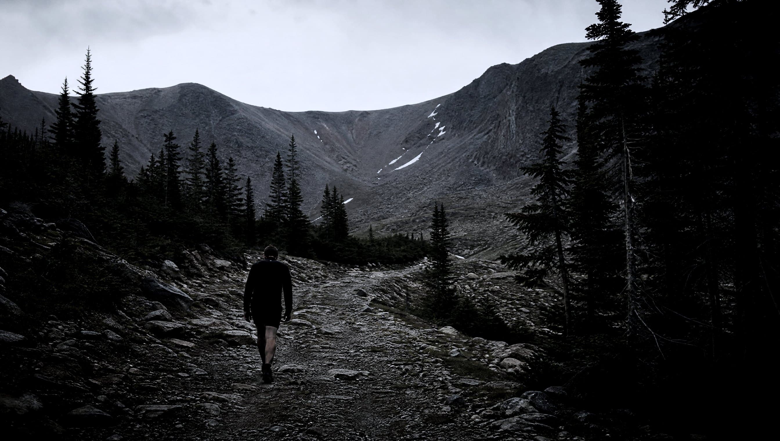 A masters-age runner power hiking a rocky jeep track through pines towards a high pass at a frosty dawn