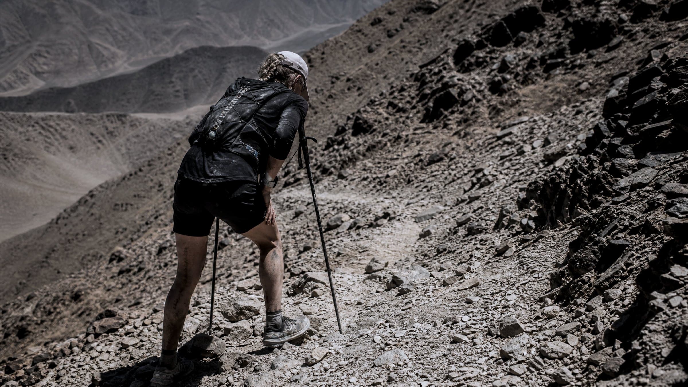 A runner hunched over poles on a long climb, deep in expedition fatigue