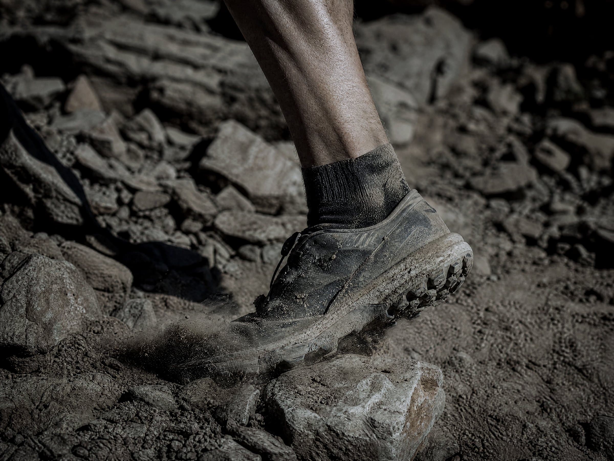 A worn trail shoe kicking up dust on a rocky fell path
