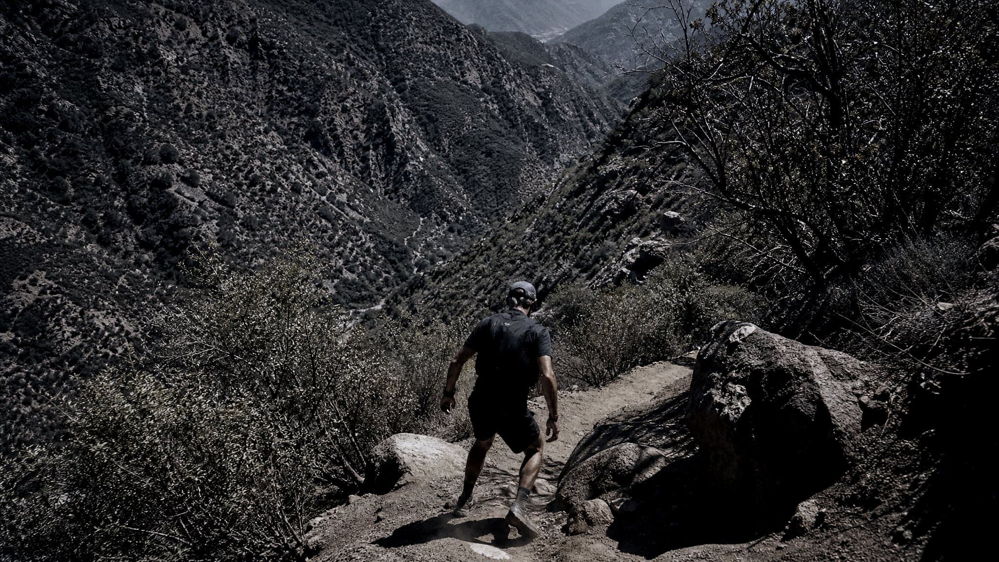 A masters-age runner descending a dusty switchback into a hot Sierra canyon at midday