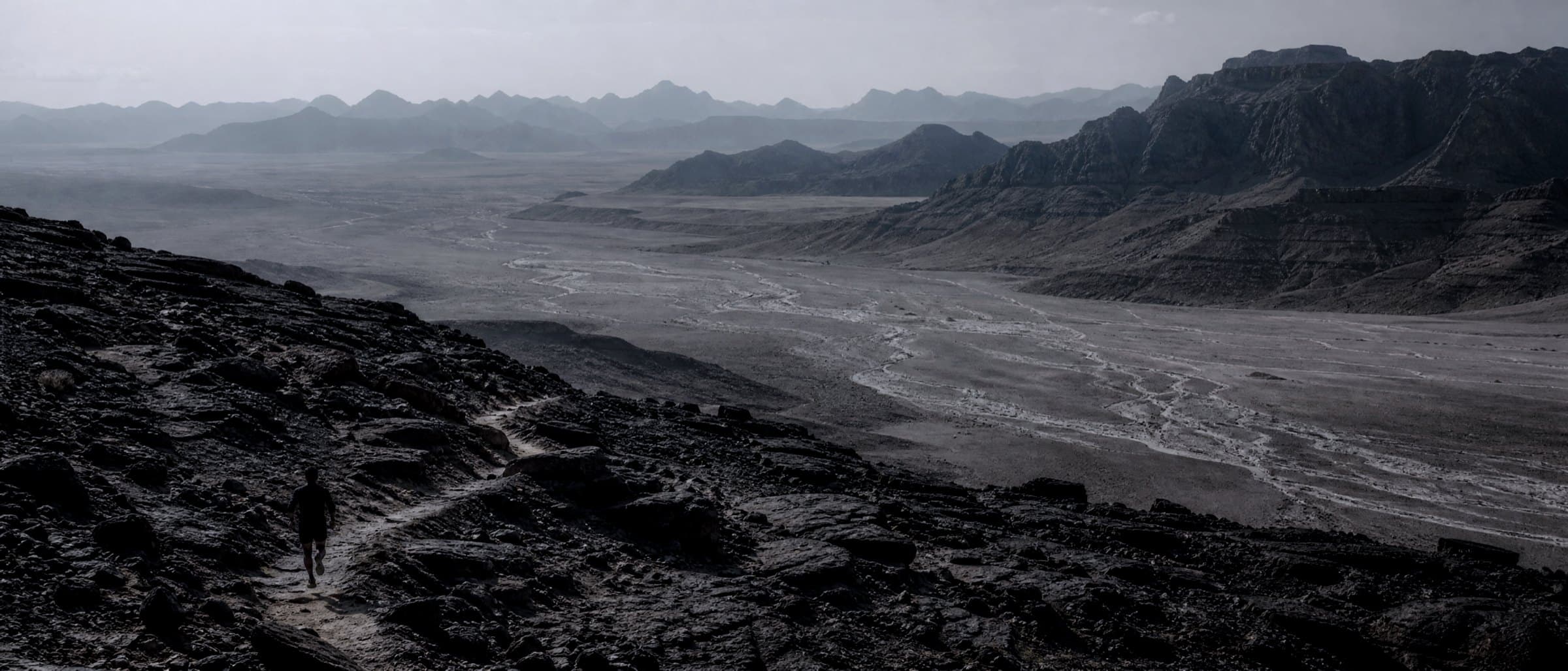 A vast desert plateau with a single tiny runner on a long exposed trail